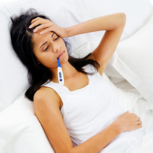 A sick woman lying in bed with a thermometer in her mouth.