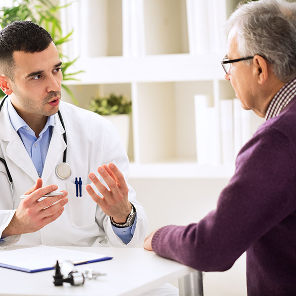 Un profesional de atención médica hablando con un paciente mayor.