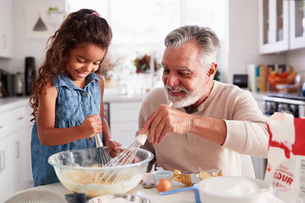 Una niña y un hombre mayor batiendo la mezcla de pastel juntos en la mesa de la cocina.