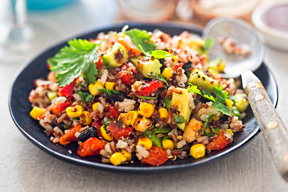 Una ensalada de frijoles negros, aguacate, maíz, tomate, arroz y quinoa.