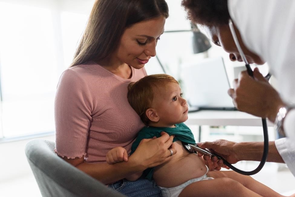 Pediatra usando un estetoscopio en un bebé que es sostenido por su madre.