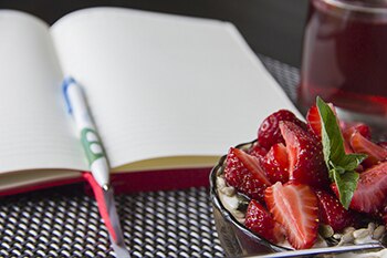 Tazón de fresas en el escritorio en la parte superior de una página en blanco de un libro diario.