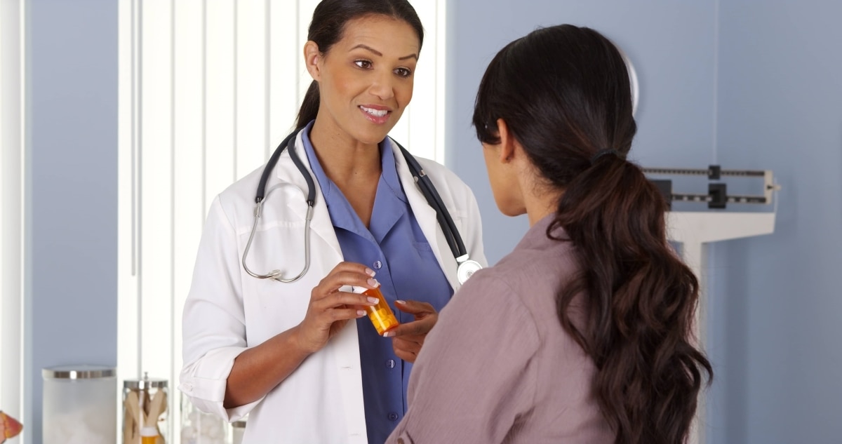 Una profesional de atención médica hablando con una paciente sobre un medicamento.