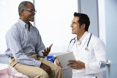 Un médico que está hablando con un paciente en la mesa de exploración del consultorio.