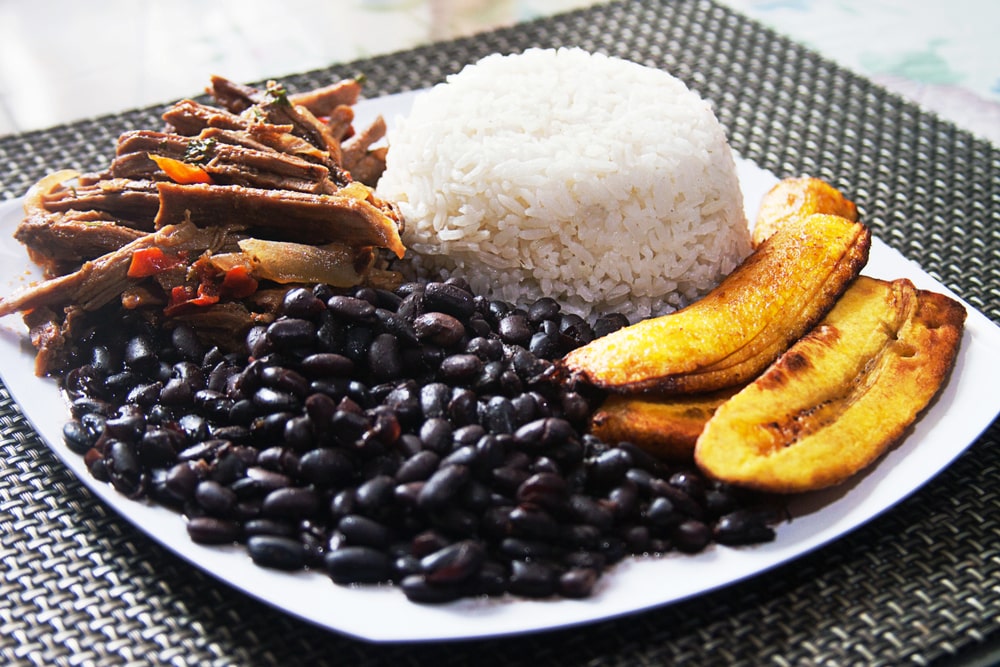 Un plato de arroz, carne desmechada, frijoles negros guisados y plátanos. 