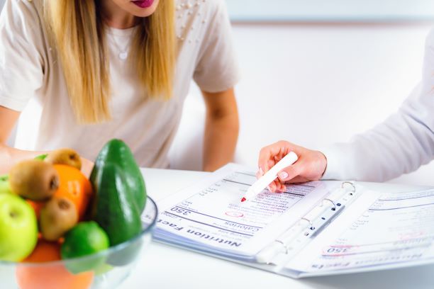 Una paciente se sienta a la par de una mesa y revisa un cuadro dietético con un profesional de la salud.