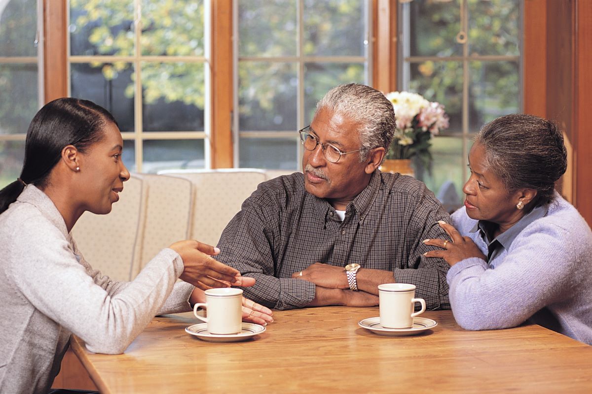 An older couple siting at a table and listening to a younger woman speak.