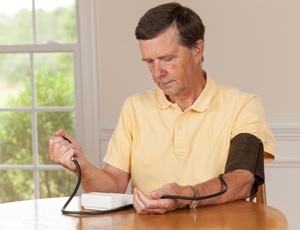 صورة لرجل كبير في السن يقيس ضغط دمه في المنزل.
