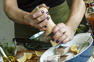 Mujer moliendo pimienta encima del pescado fresco con limón y hierbas.