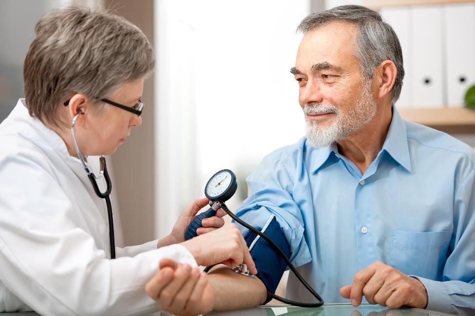Una profesional de atención médica tomando la presión arterial de un paciente mayor con un tensiómetro.