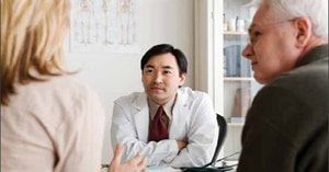 A photo of a health care provider listening to an older patient and companion.