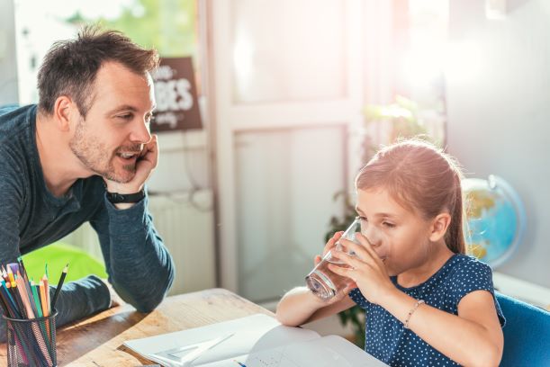 Father watching his daughter drink a glass of water while she is doing homework.