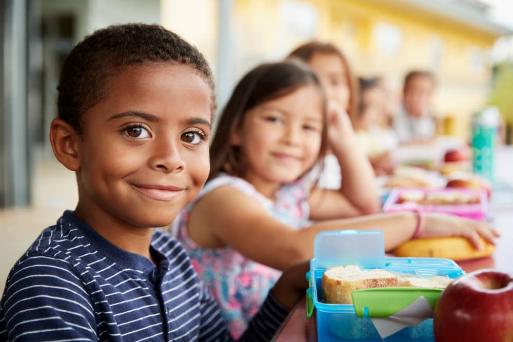 A young boy sitting at a lunch table with classmates.