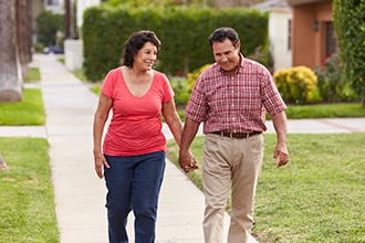 Pareja caminando sonrientes por la acera agarrados de la mano.