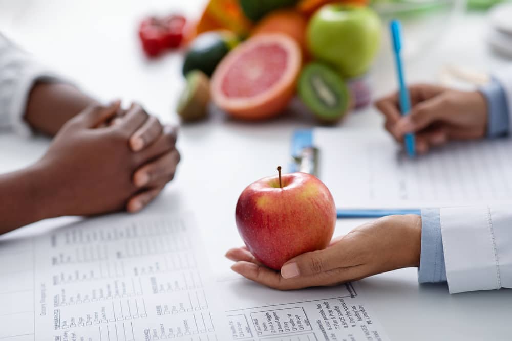 Una dietista registrada sostiene una manzana en la mano mientras aconseja a un paciente.
