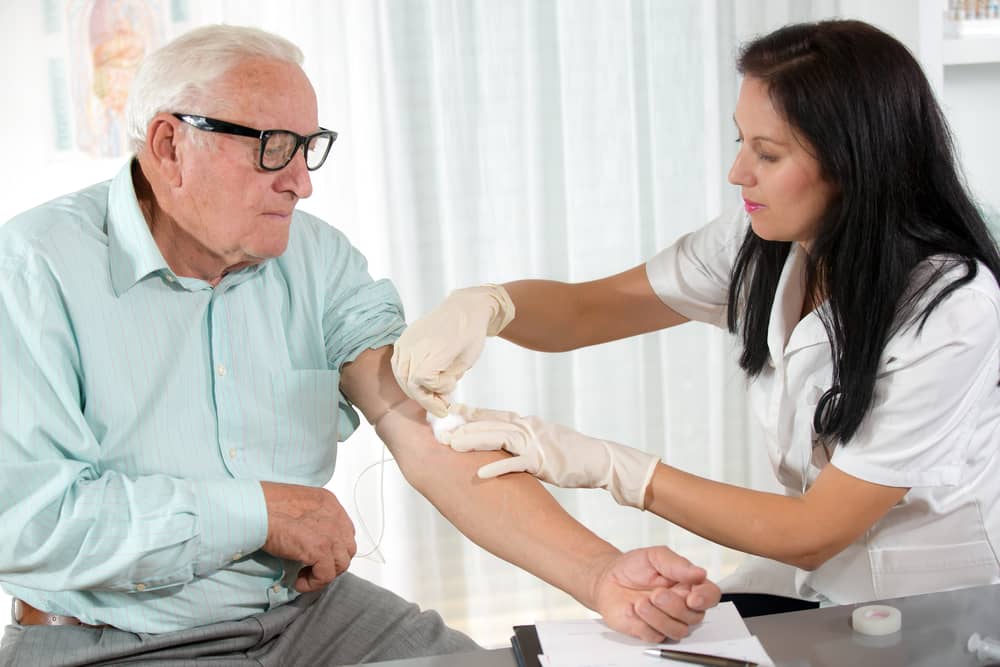 A nurse draws blood form an older man at a doctor's office.