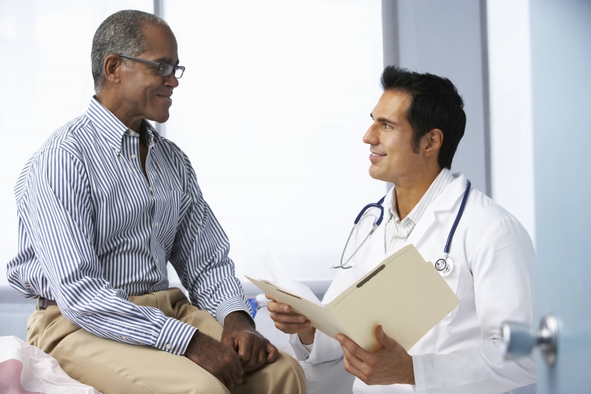 Un paciente habla con un profesional del cuidado de la salud mientras está sentado en una mesa de exploración en el consultorio médico.