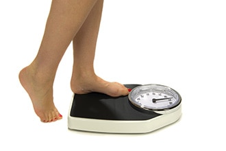 Close up of a person stepping onto a scale to weigh herself.
