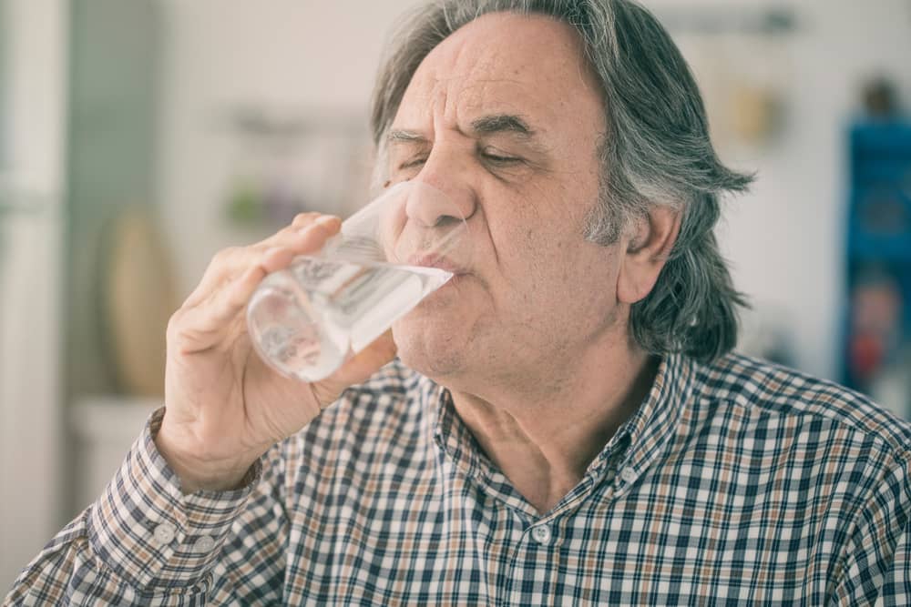 رجل كبير السن يشرب كوبًا طويلًا من الماء.