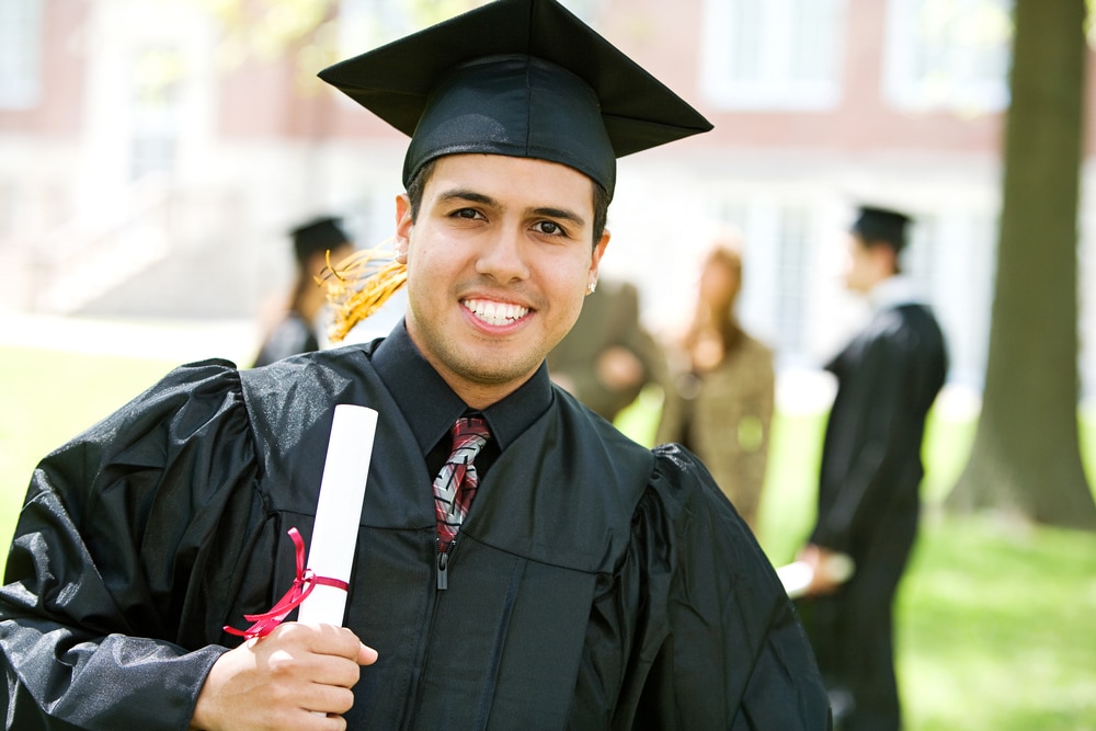 A young adult in a graduation cap and gown, smiling and holding a diploma.