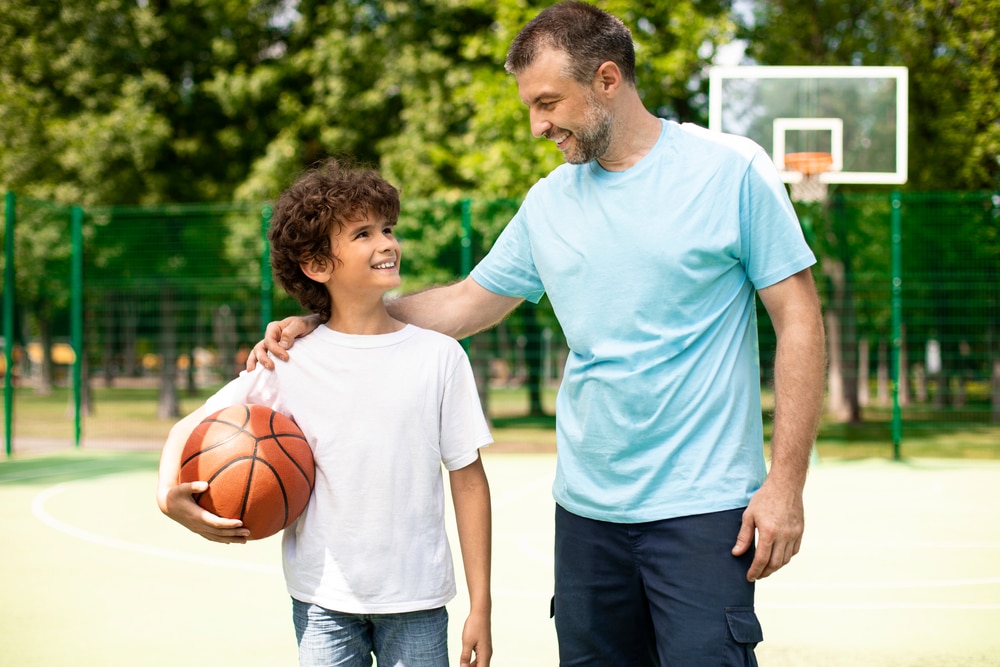 A smiling father and son on a park’s basketball court.