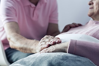 Man comforting a person who is reclining under some blankets.