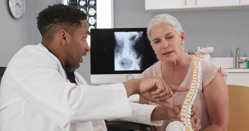 A health care professional shows a spinal model to a woman.