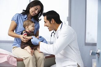 Mother holding an infant while a doctor performs a physical exam