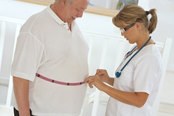 Health care professional measuring the waist of a man who has obesity.