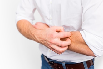 Man scratching itchy skin on his arm.