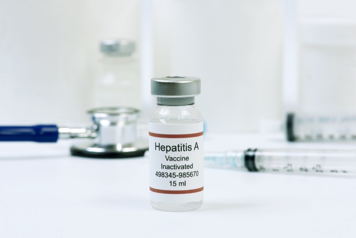 A vial containing the hepatitis A vaccine, with a stethoscope and other medical equipment in the background.