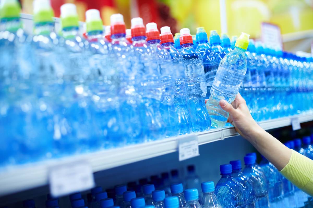 The bottled water aisle of a store with an arm coming in from the right side of the frame to select a bottle.