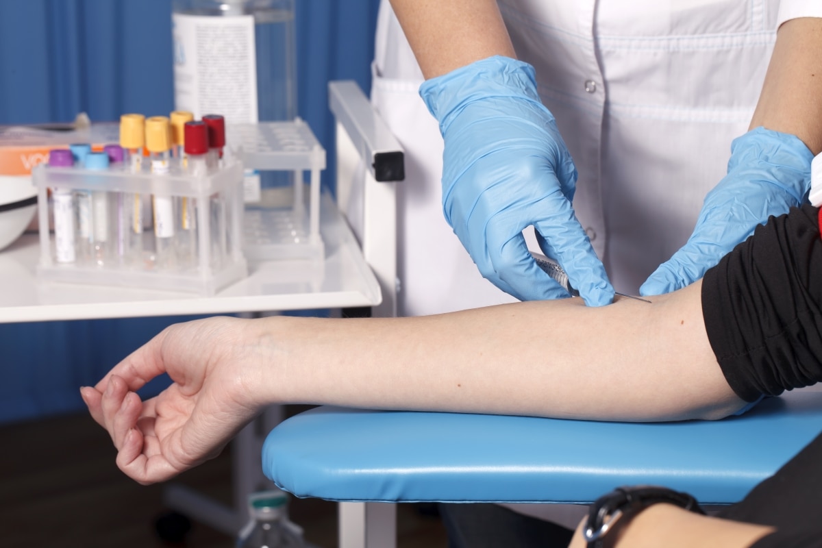 Close-up of a health care professional preparing to take a blood sample from a patient’s arm.