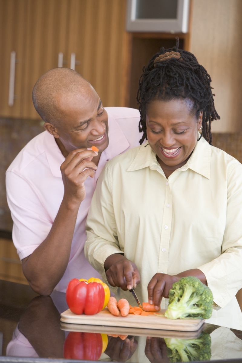 A husband and wife cutting vegetables in a kitchen.