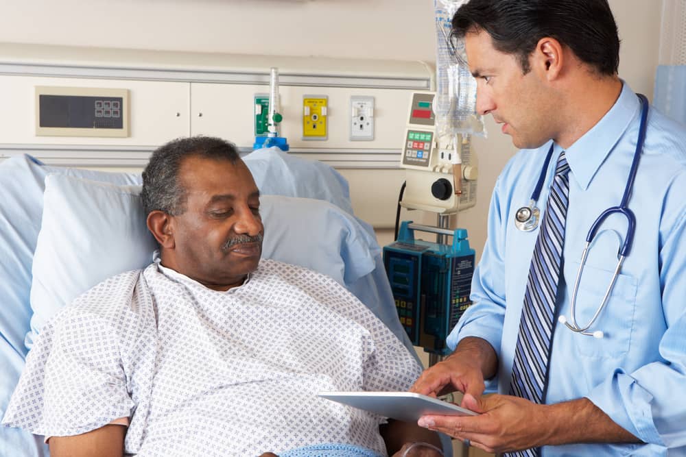Doctor habla con un paciente mayor que está acostado en una cama de hospital.