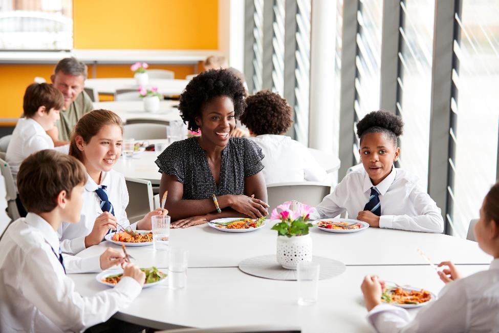 Teacher having lunch with four students at the school cafeteria.