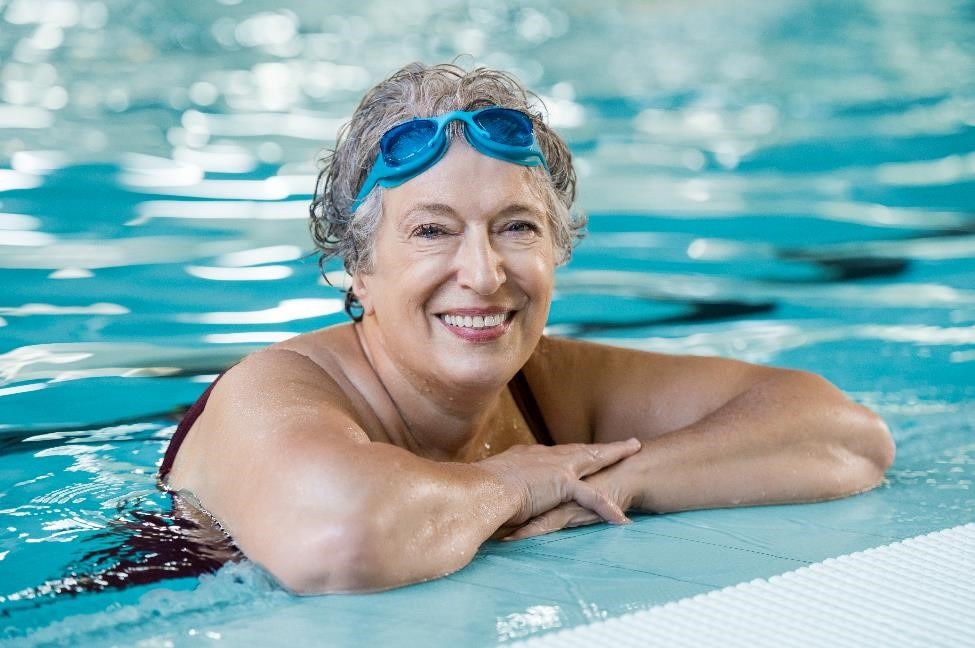A smiling woman resting at the side of a swimming pool.