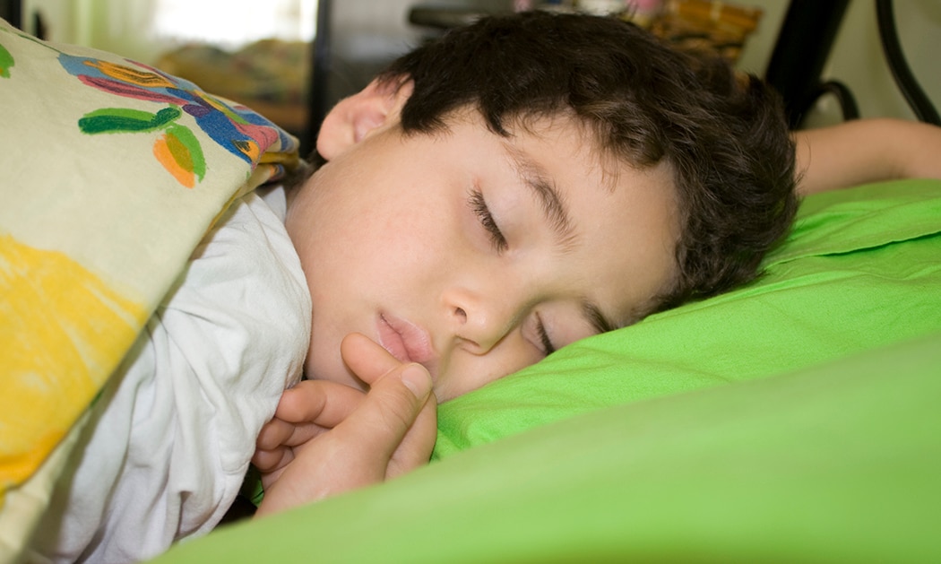 Boy sleeping under colorful blanket.