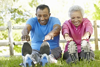 A man and a woman stretch in a park.