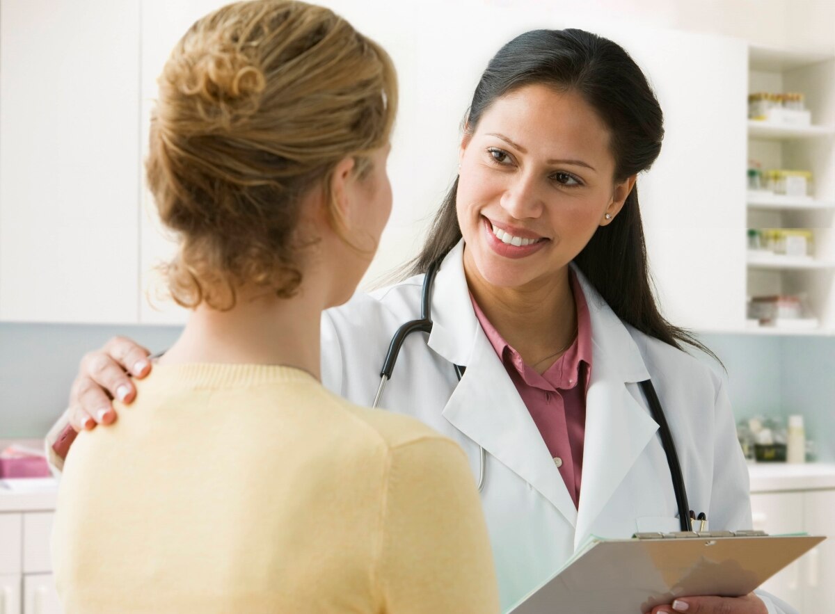 Profesional del cuidado de la salud hablando con una paciente en una sala de examinación.
