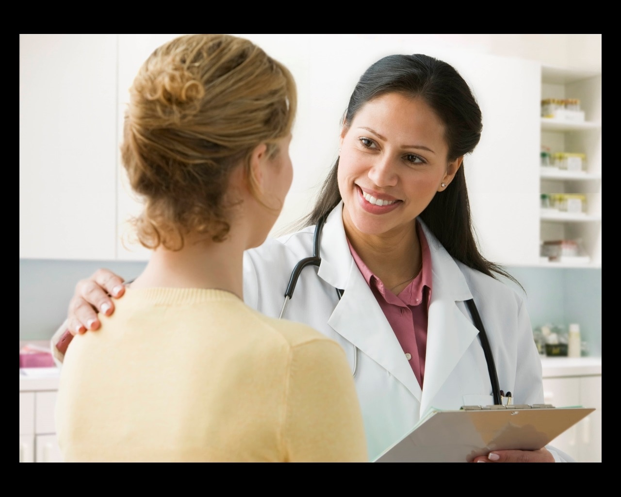 Health care professional talking with a female patient in an exam room.