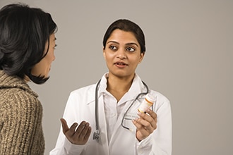 Una mujer joven habla con una profesional de la salud que lleva un estetoscopio alrededor del cuello.