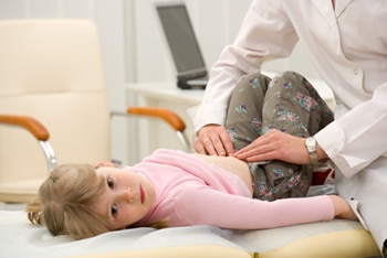 Female doctor gently touches the belly of a young girl who lies on an examining table.