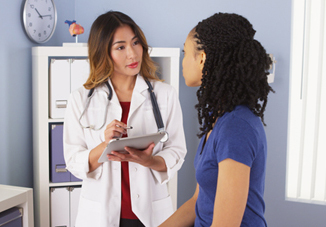 A woman sits on an examining table and talks to a health care professional.