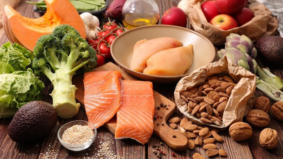 A table covered with healthy foods including broccoli, almonds, apples, salmon, tomatoes, and rice.