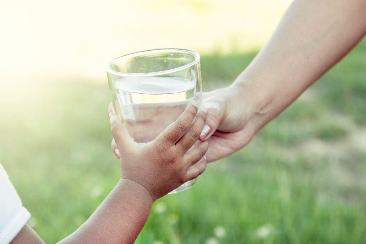 A child and adult pass a glass of water while outside.