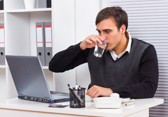 Man drinks from a large glass of water as he works on a computer.