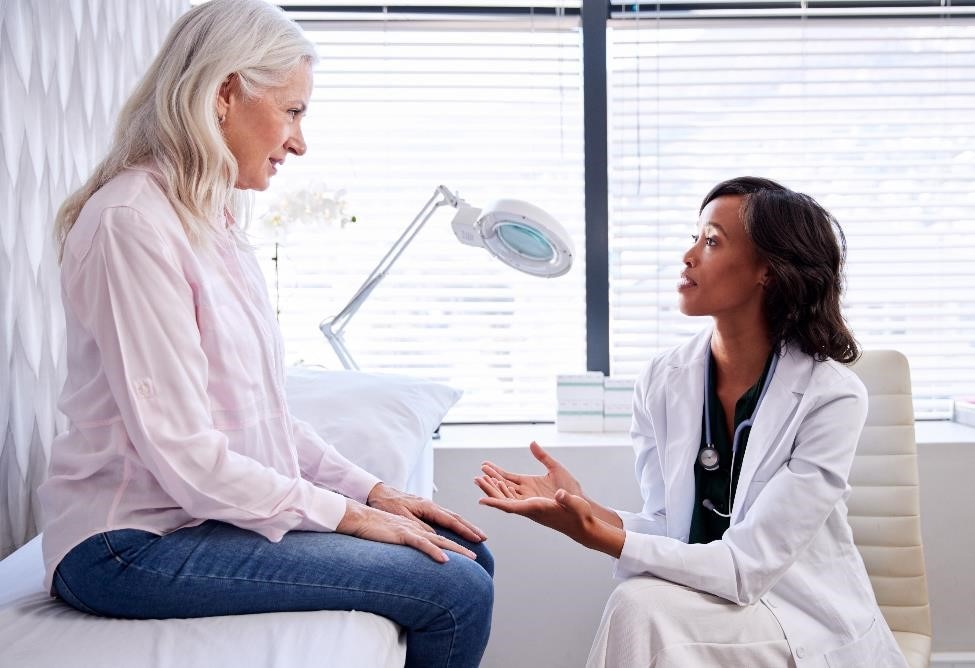 Female patient talking with a health care professional in an exam room.