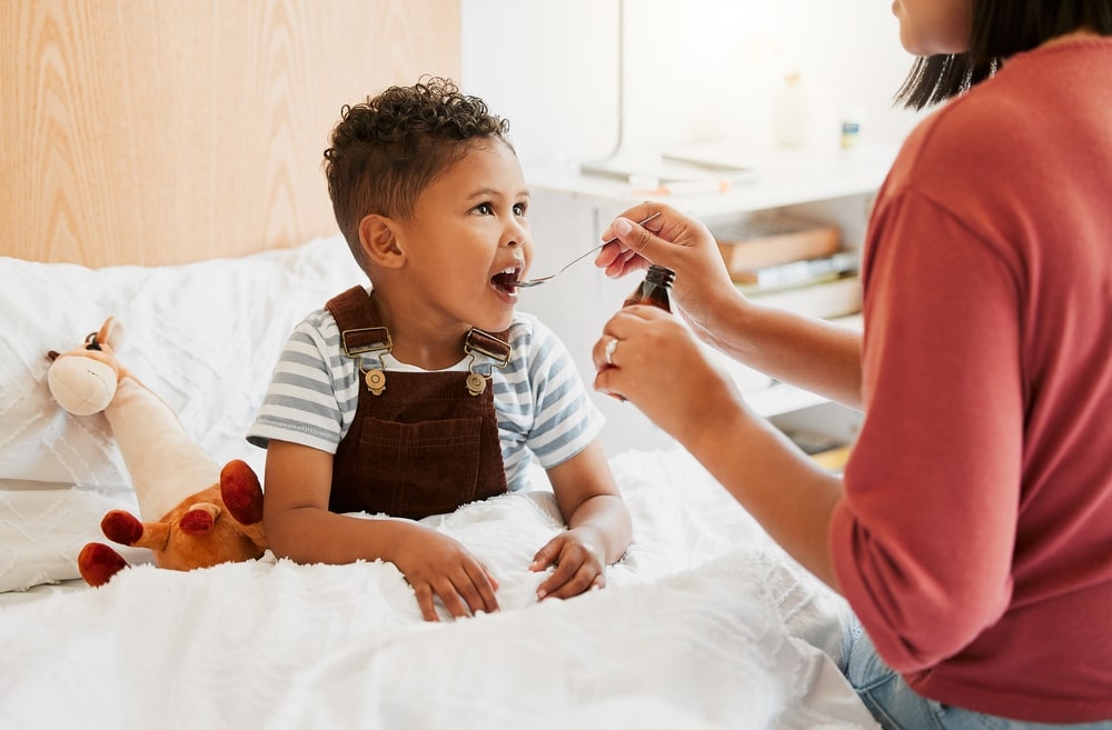 A caregiver giving a young child a spoonful of medicine.