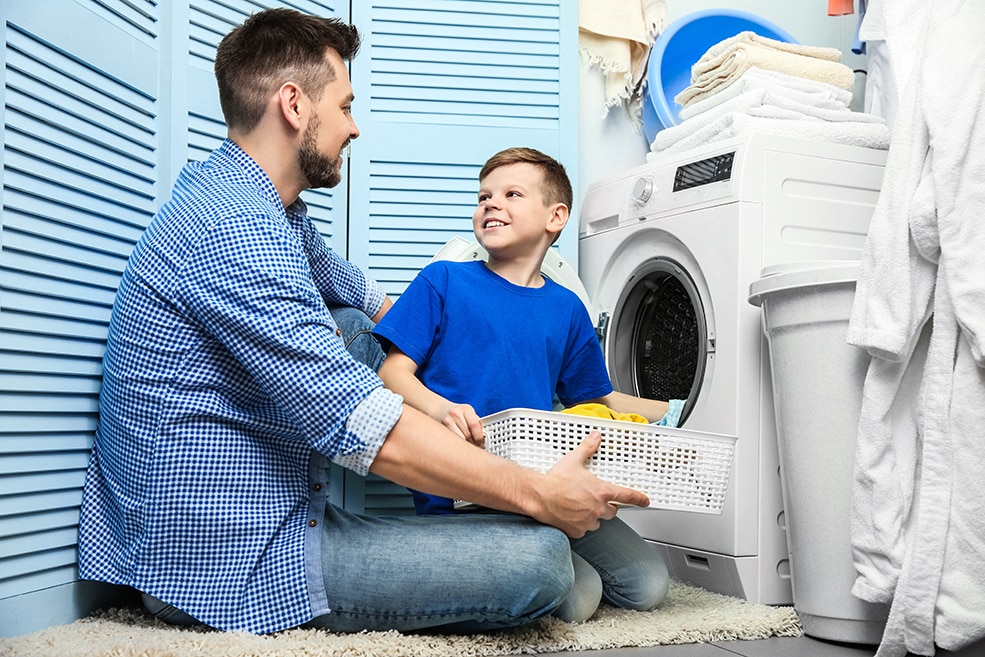 Father and son work together to put dirty laundry into a washing machine.